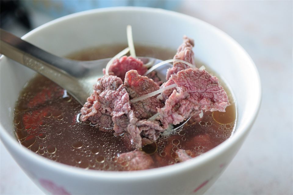 台南牛肉湯：白色瓷碗裡盛著清湯，湯中浸著粉紅色的薄切牛肉片，碗邊放著一支湯匙。